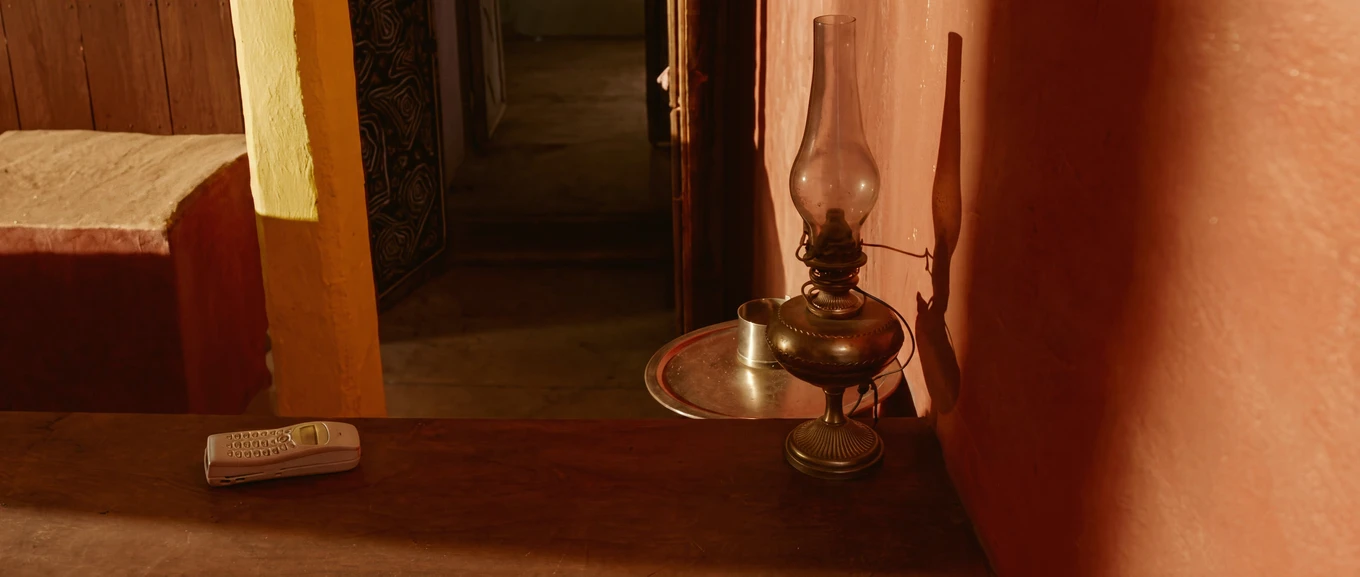A feature phone lying on a wooden counter beside an oil lamp